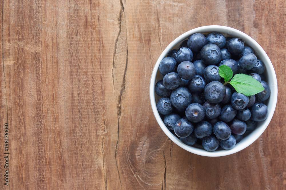Fresh ripe wild blueberries in white bowl on rustic wood table in top view flat lay with copy space for background. Blueberry is antioxidant food and vitamin C. Healthy and delicious fruits concept. Fresh ripe wild blueberries in white bowl on rustic wood table in top view flat lay with copy space for background. Blueberry is antioxidant food and vitamin C. Healthy and delicious fruits concept.