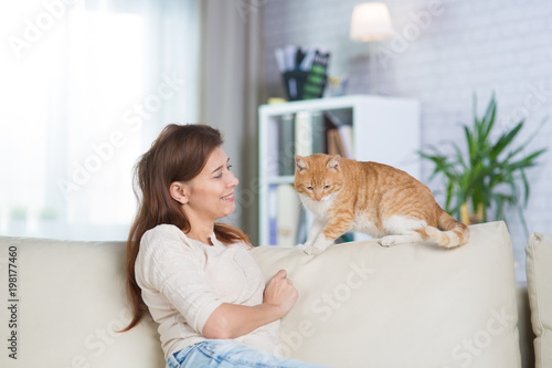 Beautiful adult woman at home on the couch with a redhead cat