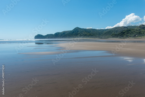 The sky and clouds reflected on the wet sand at Piha Beach New Zealand