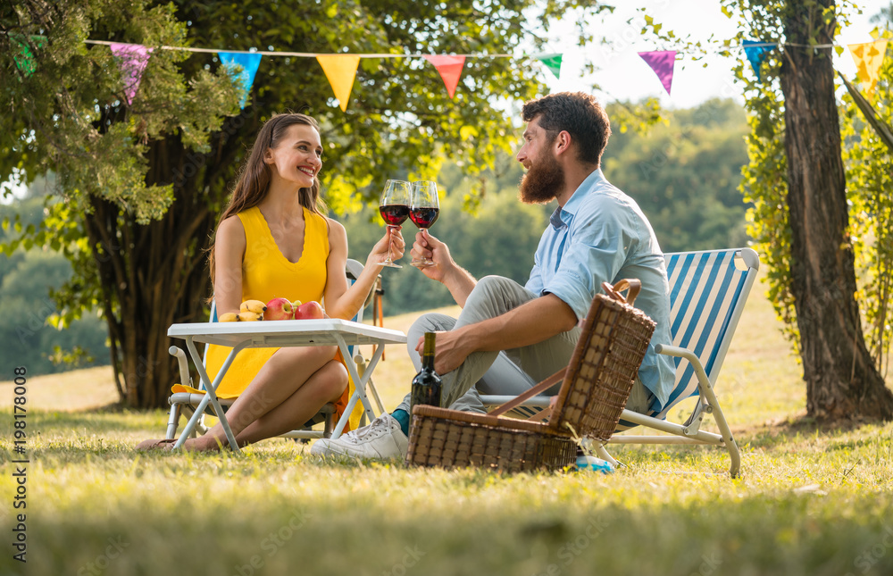 Happy young couple toasting with red wine while celebrating their love and relationship during a romantic picnic in a perfect day of summer Happy young couple toasting with red wine while celebrating their love and relationship during a romantic picnic in a perfect day of summer