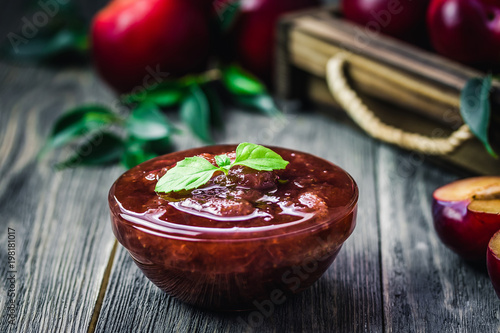 Homemade ginger plum jam in glass jar on rustic wooden background. Selective focus, space for text.