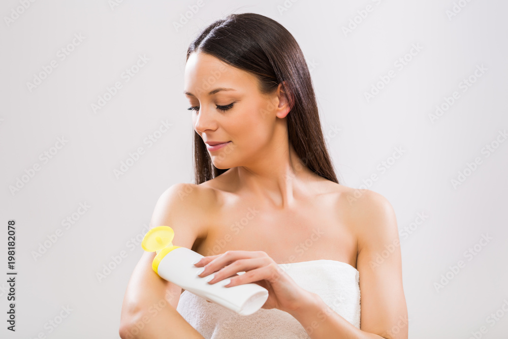 Beautiful woman applying moisturizer on her arm on gray background. Beautiful woman applying moisturizer on her arm on gray background.