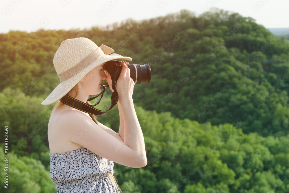 Girl in hat takes pictures against the background of green mountain. Side view