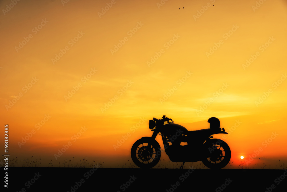 Silhouette of motorcycle parking with sunset background in Thailand,Young Traveller man place helmet on motorbike.Trip of Motorcycle Concept.
