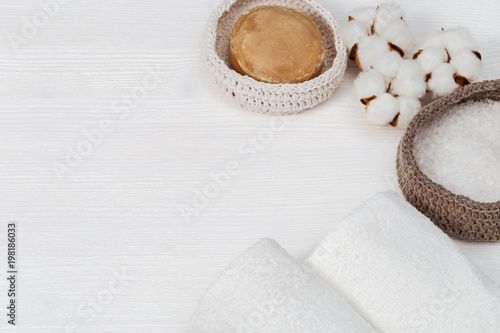 Spa set. Items for spa on white wood background with copy space. Top view spa concept with bath salt in knitted box, cotton flowers, soap, clean white towels.