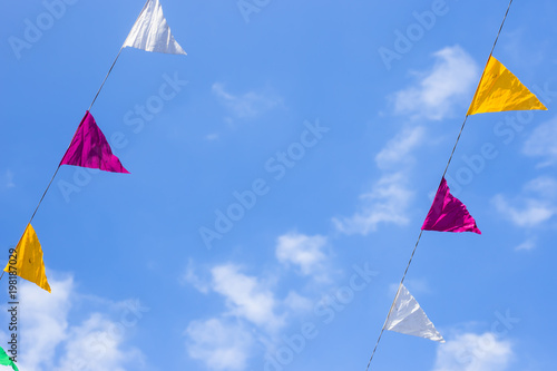 Multi-colored flags decoration hanging on a background of blue sky with white clouds. Copyspace