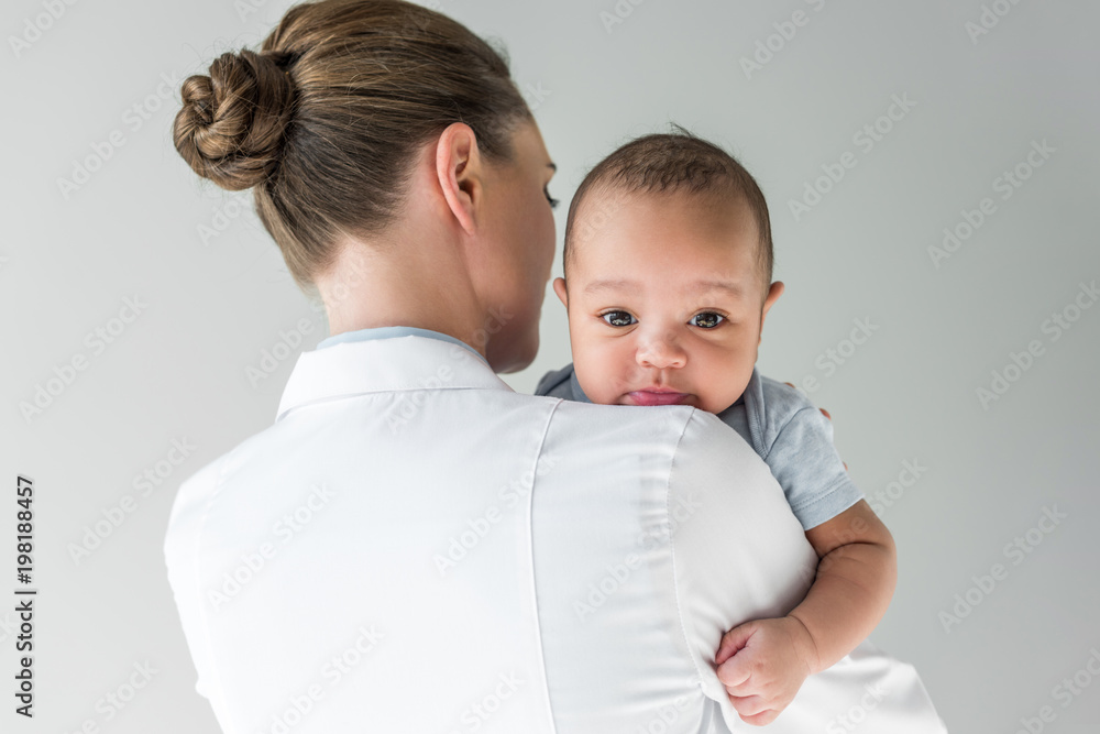 rear view of female pediatrician with african american baby isolated on grey rear view of female pediatrician with african american baby isolated on grey
