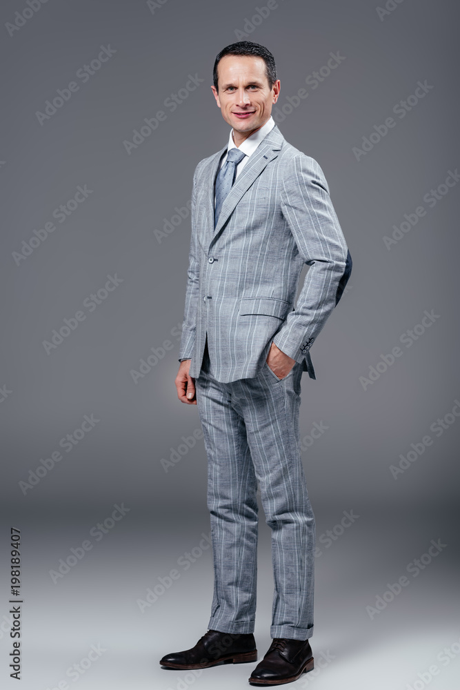 adult businessman in stylish suit looking at camera on grey adult businessman in stylish suit looking at camera on grey