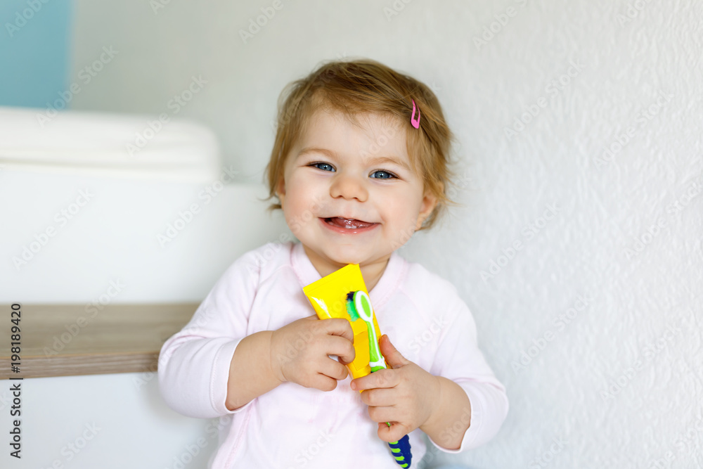 Little baby girl holding toothbrush and brushing first teeth. Toddler learning to clean milk tooth.
