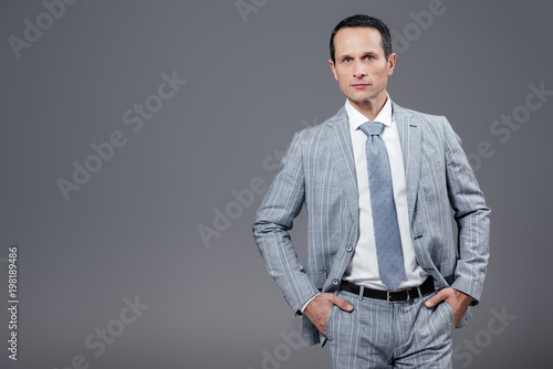 handsome adult businessman in stylish suit looking at camera isolated on grey