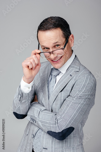 smiling adult businessman looking at camera over glasses isolated on grey