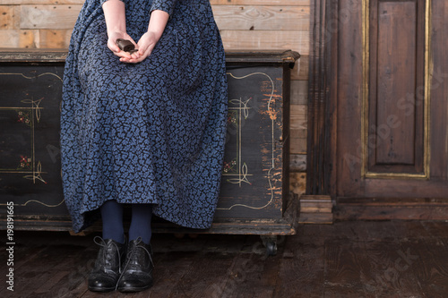 A woman in a long blue dress is sitting on a black chest and holding an old lock with a key