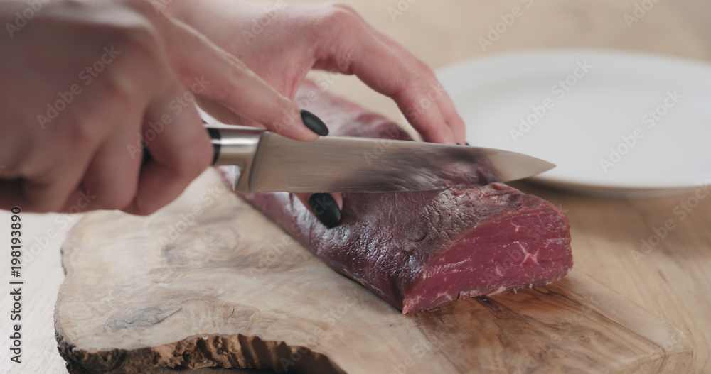 female hands slicing raw beef fillet for steak on wooden board