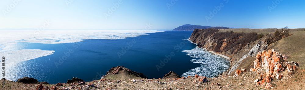 Lake Baikal in May sunny day. Panoramic view from the cliffs of Olkhon Island to white ice floes on blue water during the spring ice drift Lake Baikal in May sunny day. Panoramic view from the cliffs of Olkhon Island to white ice floes on blue water during the spring ice drift
