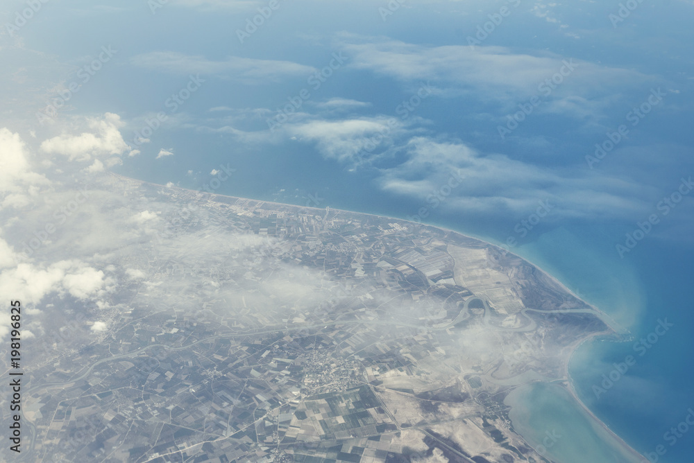 Top view from landing airplane. Window plane with copy space. Aerial view of cloud, sea, ocean and city landscape