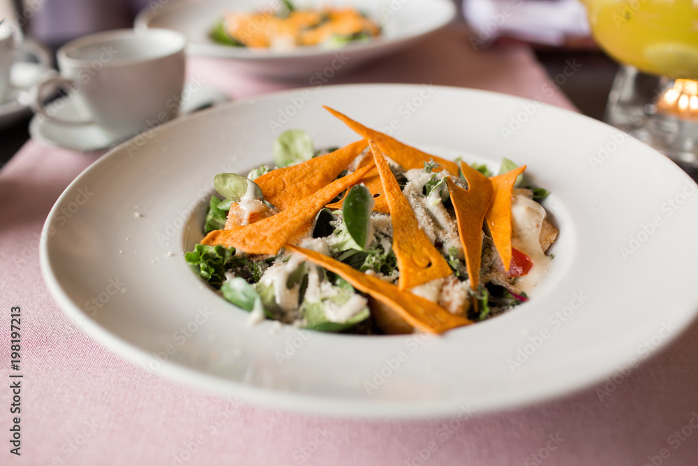 Caesar salad with chicken, greens and crispy chips on the table. Business lunch with a beautiful pineapple-orange tea in a glass teapot. Caesar salad with chicken, greens and crispy chips on the table. Business lunch with a beautiful pineapple-orange tea in a glass teapot.