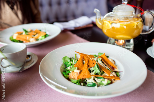 Caesar salad with chicken  greens and crispy chips on the table. Business lunch with a beautiful pineapple-orange tea in a glass teapot.