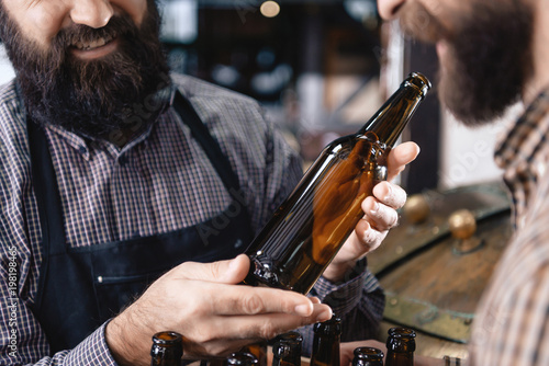 Bearded man holds empty bottle intended for craft beer near brewery. Empty beer bottle.