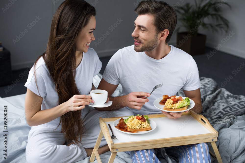 Beautiful young couple drinking coffee and eating breakfast in bed Beautiful young couple drinking coffee and eating breakfast in bed