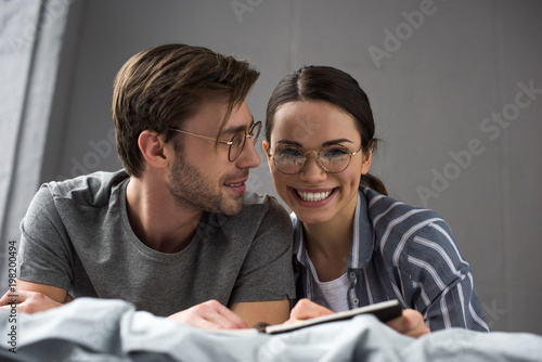 Happy man and woman writing in notepad while lying in bed