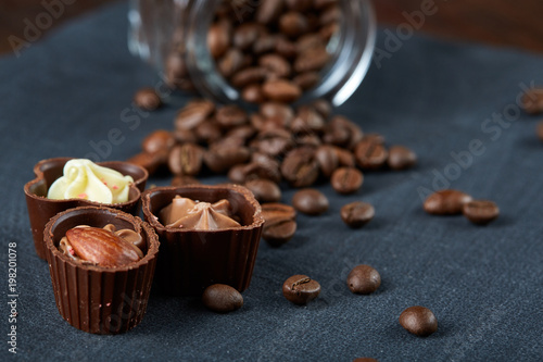 Side view of overturned glass jar with coffee beans and chocolate candies on wooden background, selective focus photo