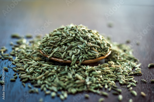 Raw dried fennel seeds or variyali or Foeniculum vulgare in a brown plate on wooden surface.
