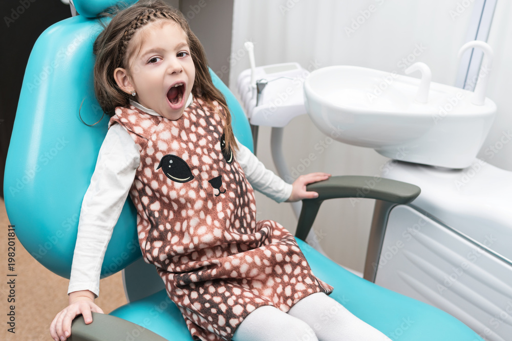 Little girl sitting in a dental chair with an open mouth Little girl sitting in a dental chair with an open mouth