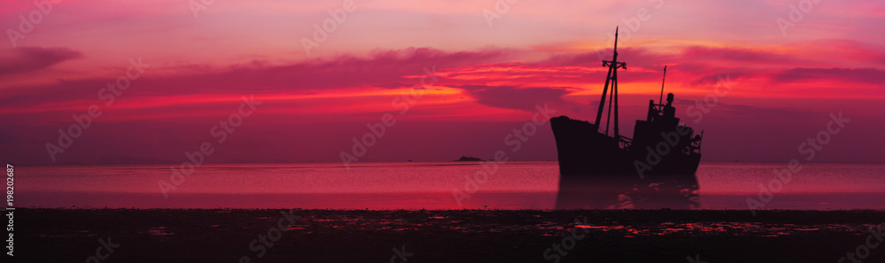 Silhouette of a crashed ship in sea. Sunset over the sea. Panorama