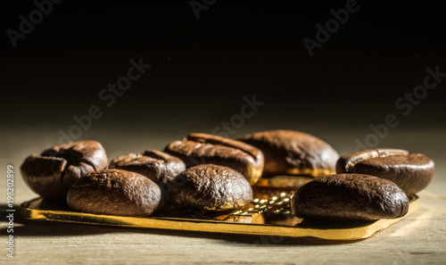 Several roasted coffee beans on a smol bar of gold. On a dark background. Selective focus.