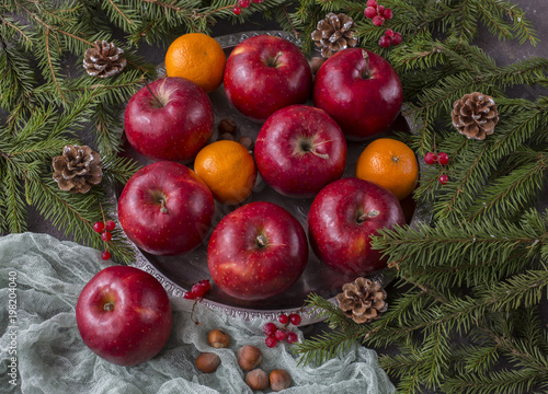 on a table in a silver plate are red apples  mandarins  cones and pine branches