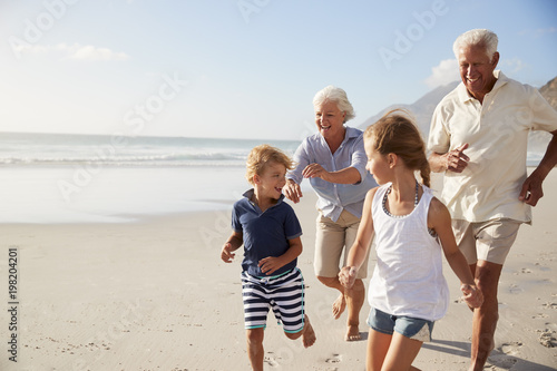 Grandparents Running Along Beach With Grandchildren On Summer Vacation