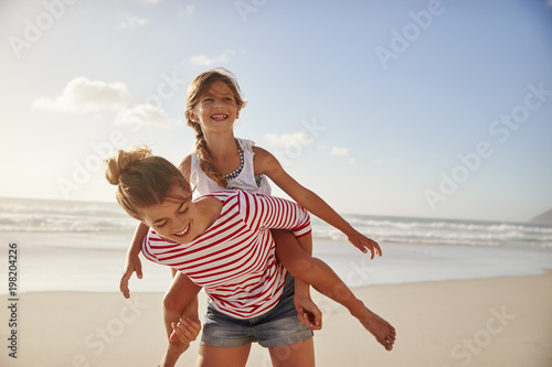 Mother Carrying Daughter On Shoulders On Beach Vacation