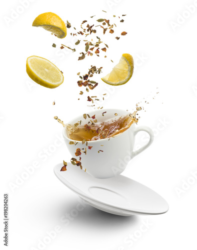cup of tea jumps with herb tea and lemon slices splashing on white background