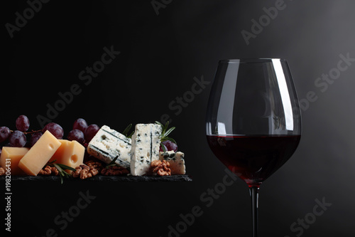 Glass of red wine with various cheeses , grapes and walnuts .