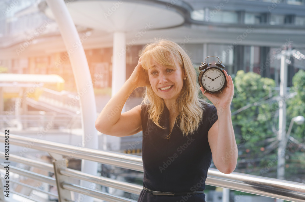 portrait of woman surprised and Shocked with holding clock at outdoor in modern city on morning. clock and time concept.