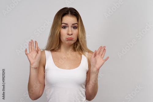 Young woman with long blond hair in white tank top stands on isolated background. Beautiful girl shows that she is not guilty 