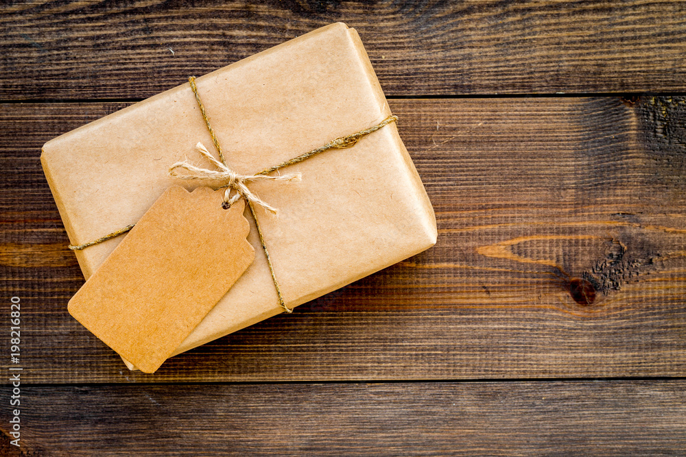 Parcel packaging box wrapped with craft paper with empty label mockup on dark wooden background top view copy space Parcel packaging box wrapped with craft paper with empty label mockup on dark wooden background top view copy space