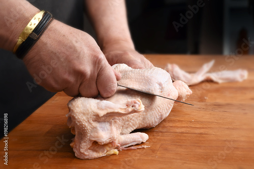 Male hands prepare a raw chicken with a kitchen knife for cooking on a rustic wooden butcher block