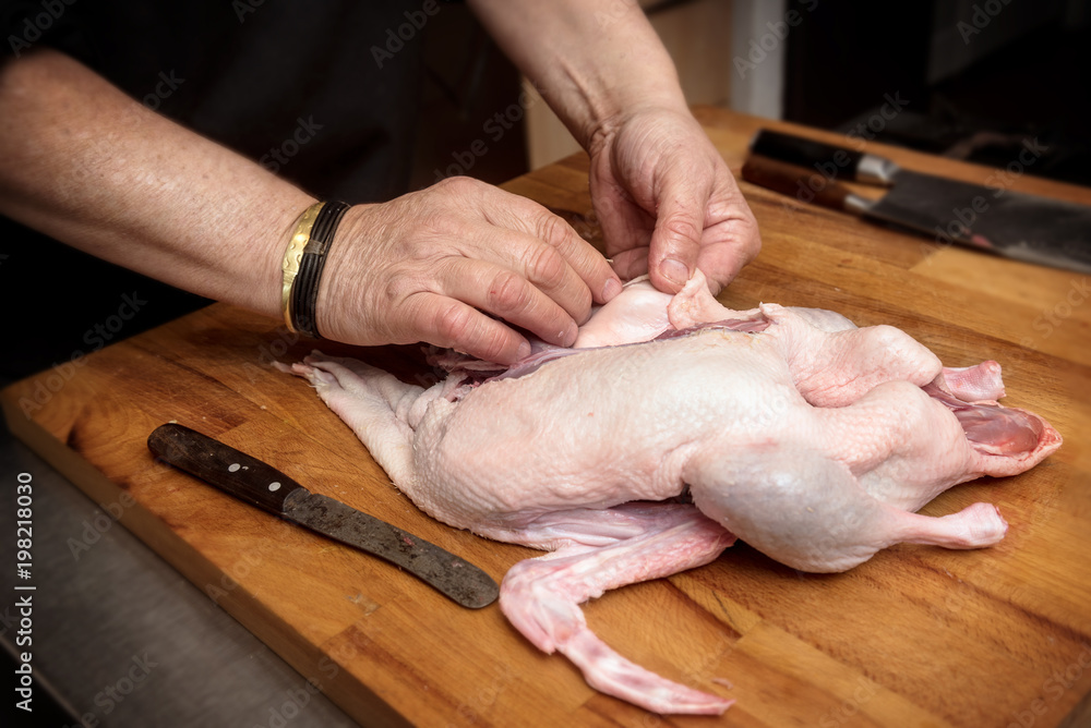 male hands prepare a raw duck for cooking on a rustic wooden butcher block