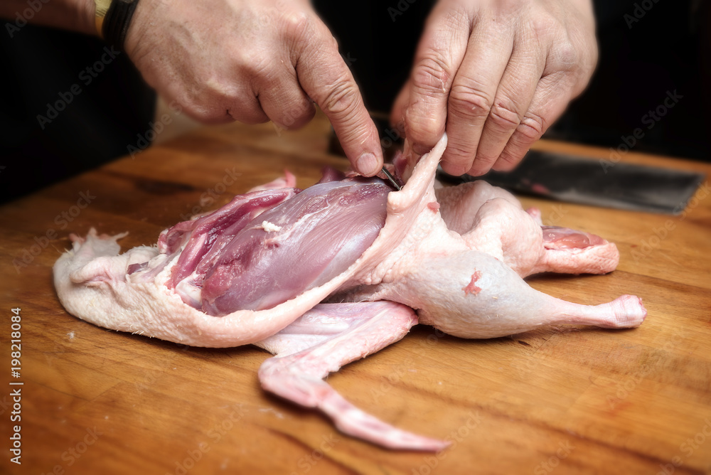 male hands prepare a raw duck to get the breast fillet for cooking on a rustic wooden butcher block