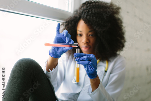 Young beautiful African American girl doctor in a white coat with a stethoscope. sitting at a table with reagent flasks on white background. Researcher researching in the laboratory