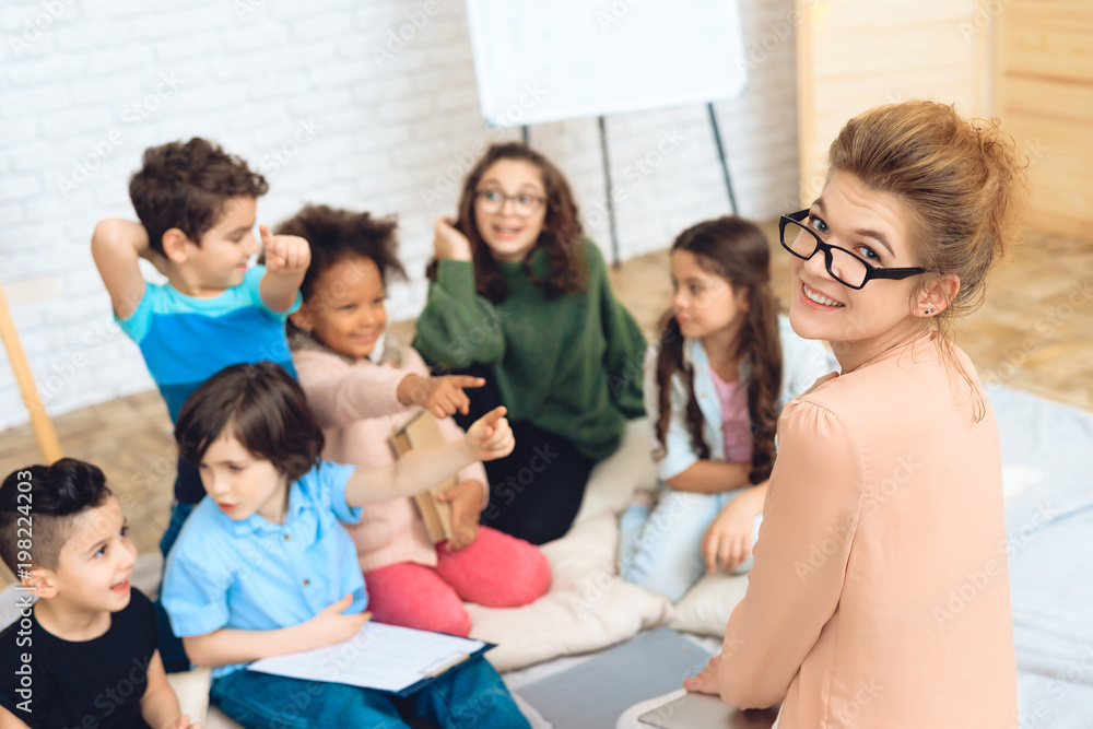 Group of children play a quiz with teacher in peach blouse while in primary school class.