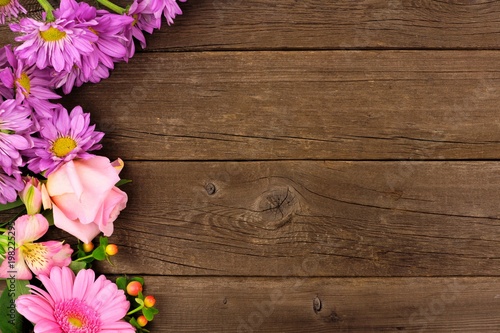 Side border of pink and purple flowers with rose, daisies and lilies against a rustic wood background. Copy space.