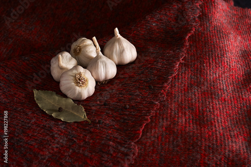 garlic, black pepper and bay leaf on dark red textile background photo