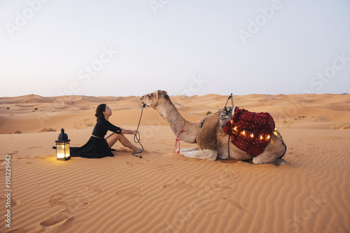 Side view of woman with camel sitting on sand at Sahara Desert against clear sky photo