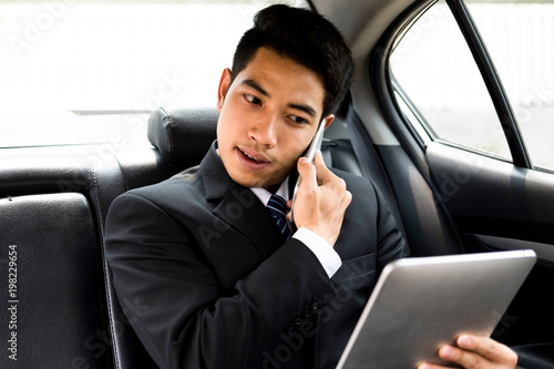 Busy businessman using mobile phone and tablet in car.