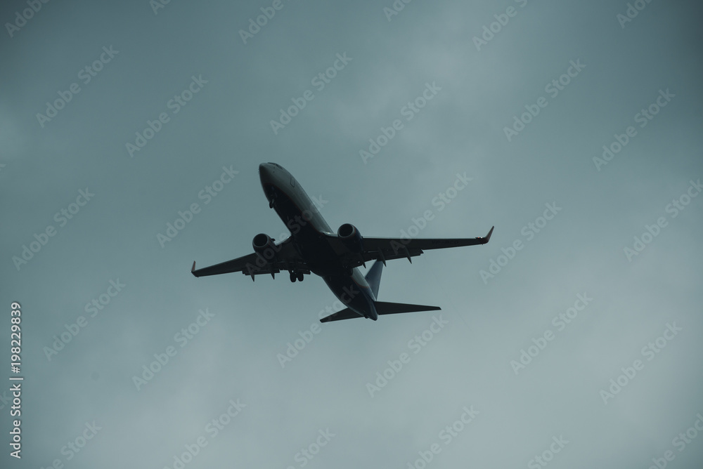 Silhouette of plane in grey sky. Passenger plane flies high in sky, flight. International flights, delivery, transportation. Flight and weather conditions concept. Silhouette of plane in grey sky. Passenger plane flies high in sky, flight. International flights, delivery, transportation. Flight and weather conditions concept.