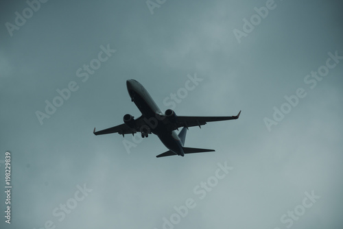 Silhouette of plane in grey sky. Passenger plane flies high in sky, flight. International flights, delivery, transportation. Flight and weather conditions concept.