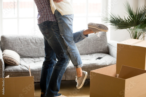 Happy couple on moving day concept, man lifting woman standing among cardboard boxes starting living together in new own house, husband holding embracing wife celebrating relocation, close up view © fizkes