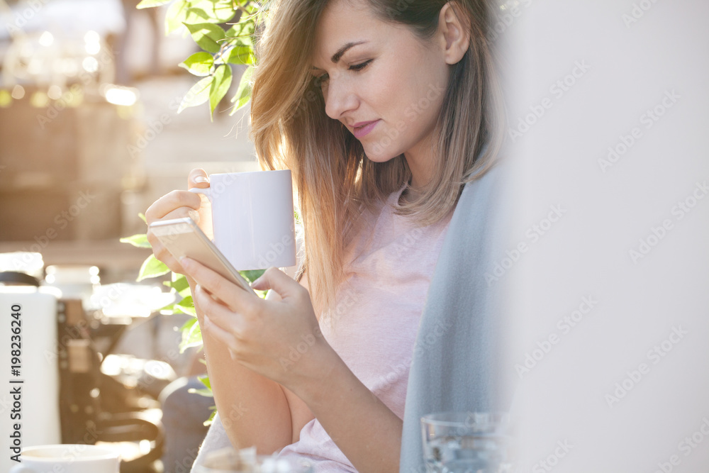 Woman enjoys morning coffee, using smart phone and relax. Beautiful sunny day, backlight Woman enjoys morning coffee, using smart phone and relax. Beautiful sunny day, backlight